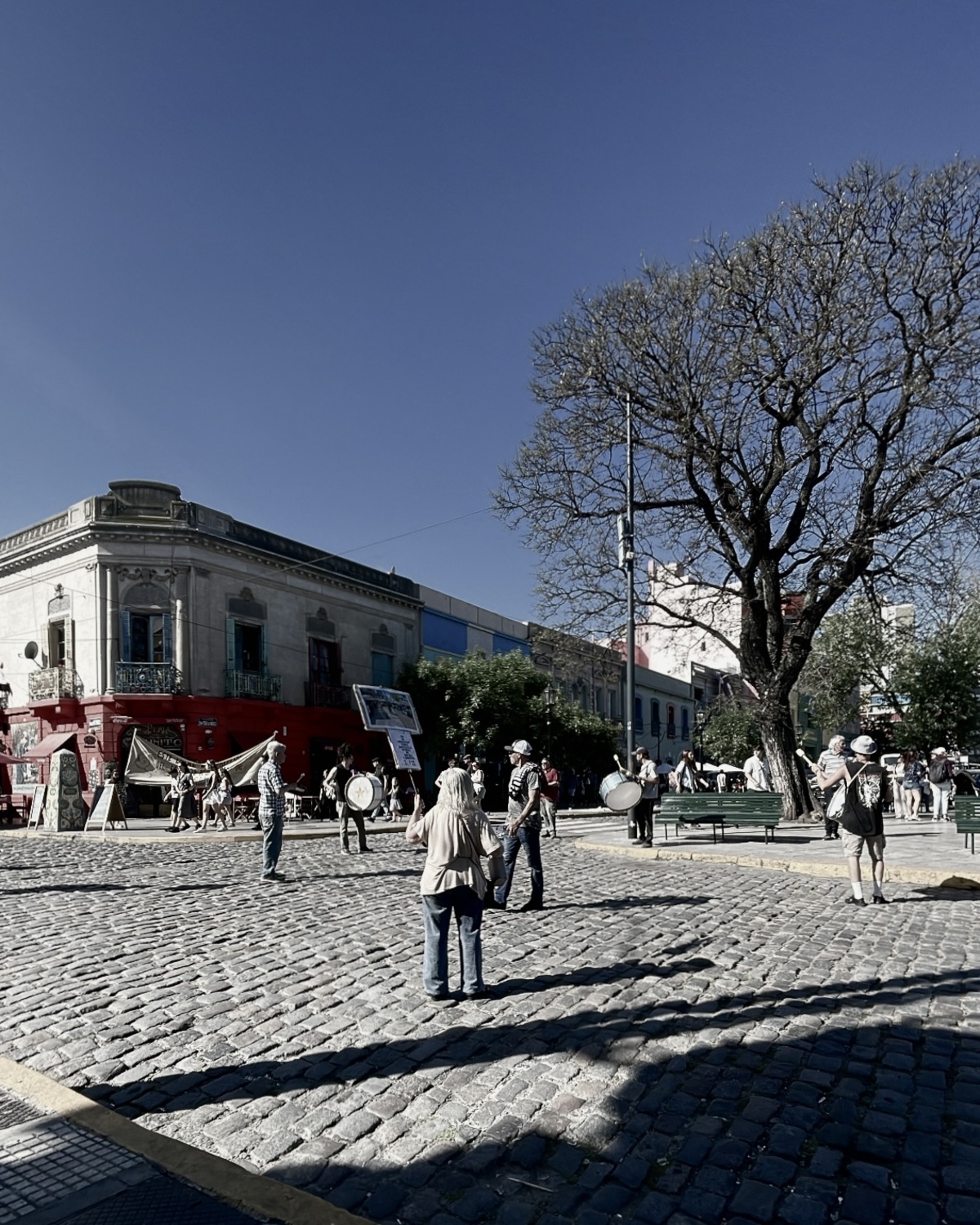 Eine Demonstration mit Transparenten und Trommeln zieht über eine Straßenecke aus Kopfsteinpflaster.